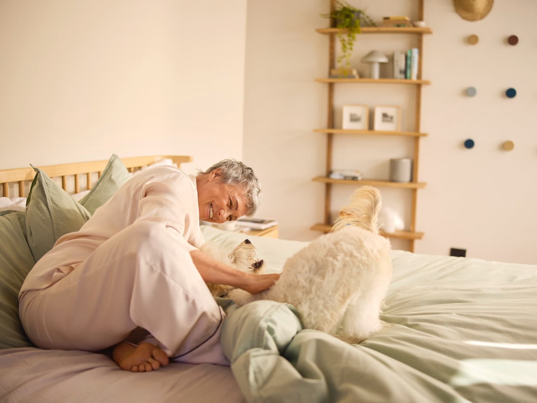 En smilende kvinde, der klapper en hund på en seng