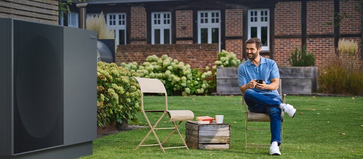 En mand, der sidder ved siden af aroTHERM, optræder i haven