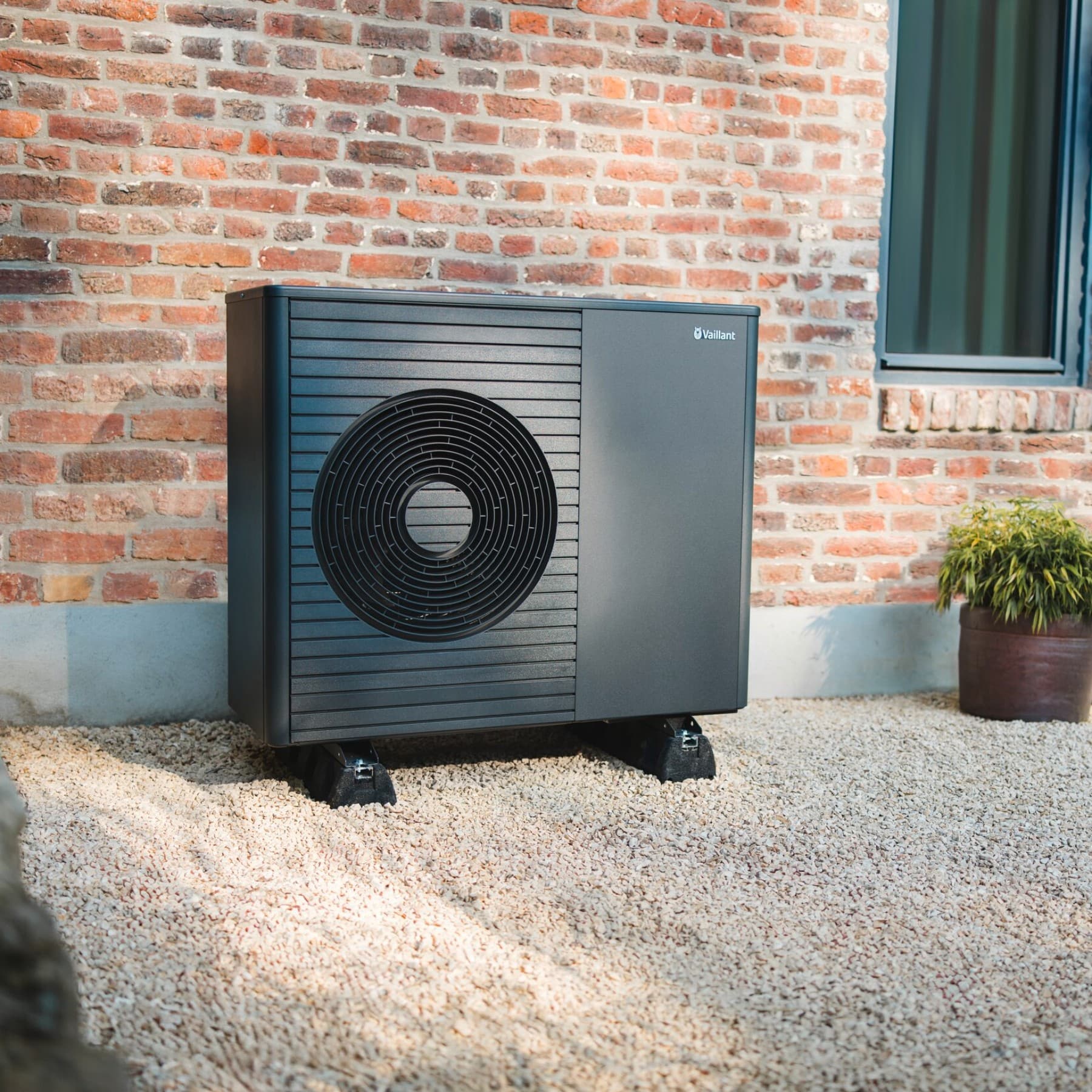 En varmepumpe står foran en ny bygning med en velplejet græsplæne og en sti i forgrunden.
