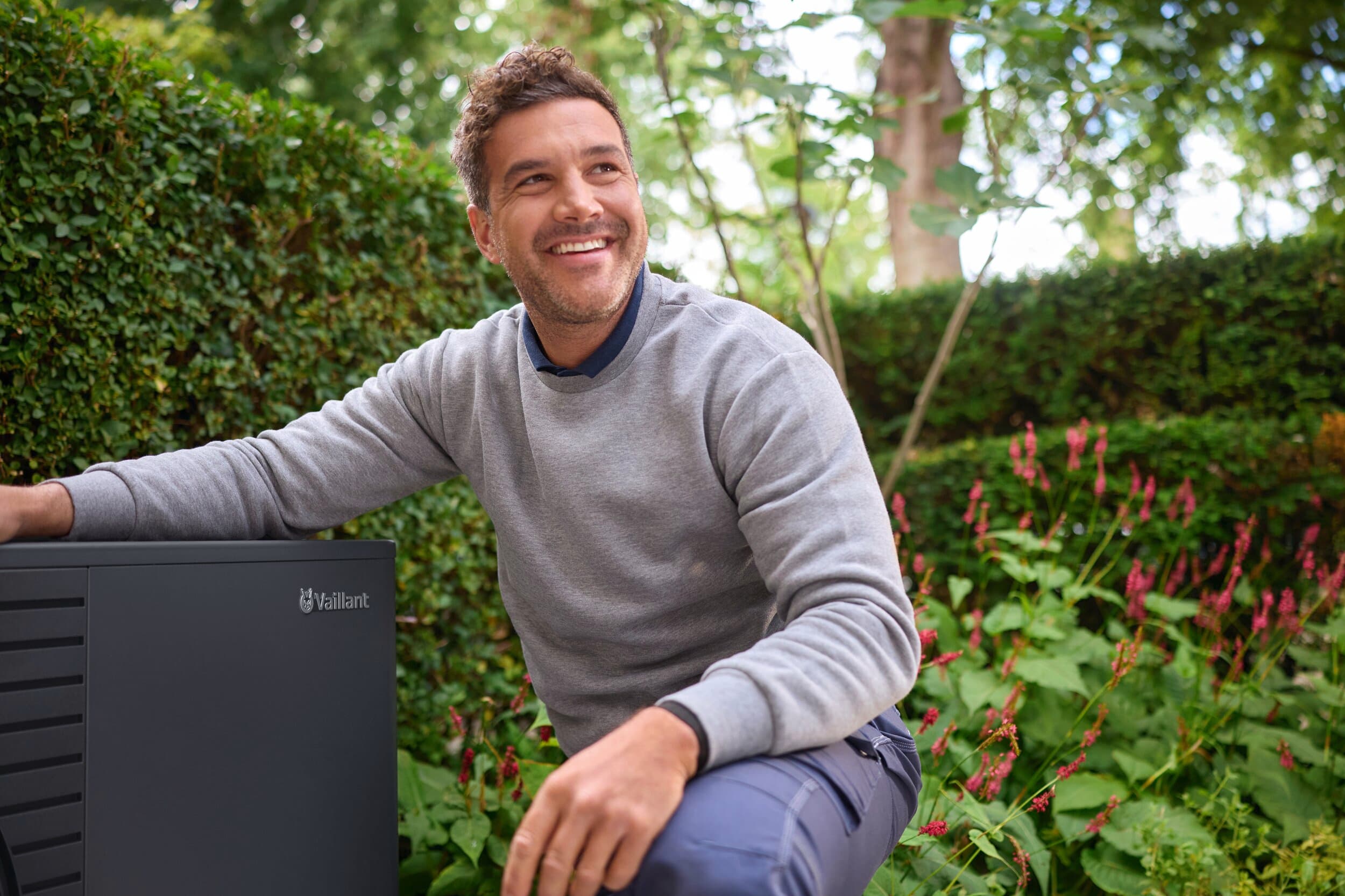 En mand, der knæler ved siden af en aroTHERM pro i haven
